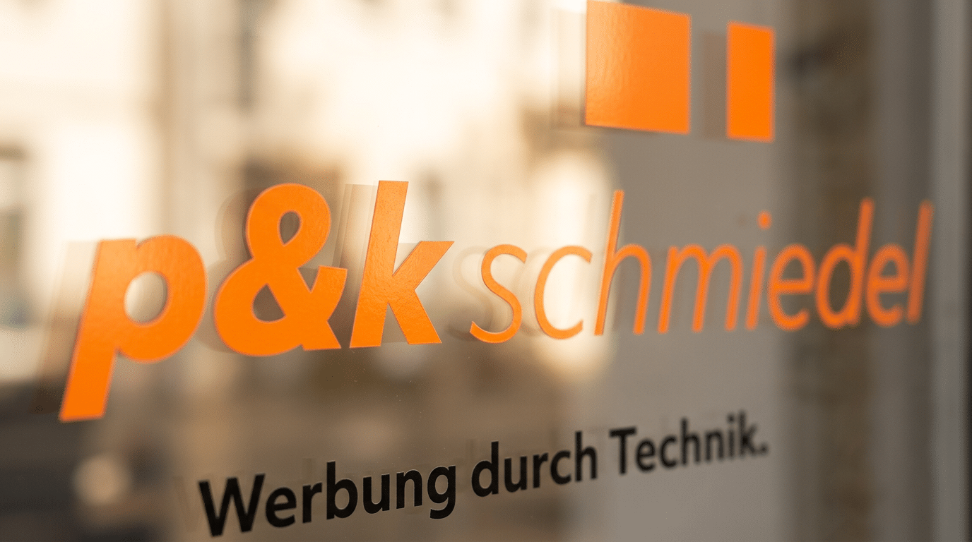 Nahaufnahme einer orangen Folienschrift auf einer Glasscheibe – professionelle Schaufensterbeschriftung von p&k schmiedel in Braunschweig